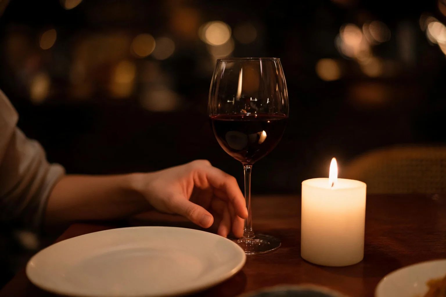A lit candle, a glass of red wine, and a plate on a table.