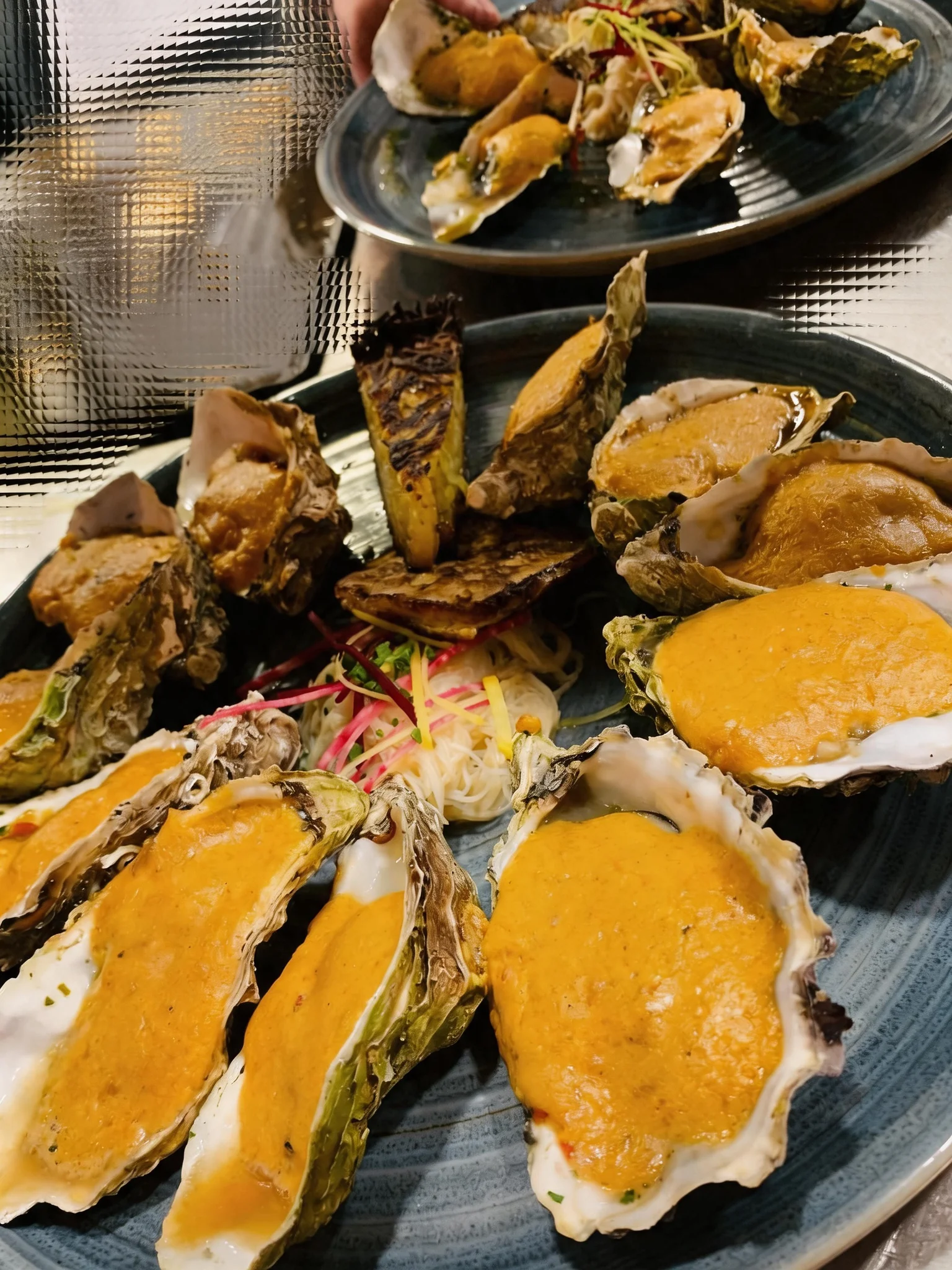 Several oysters topped with an orange-coloured sauce, on a plate.