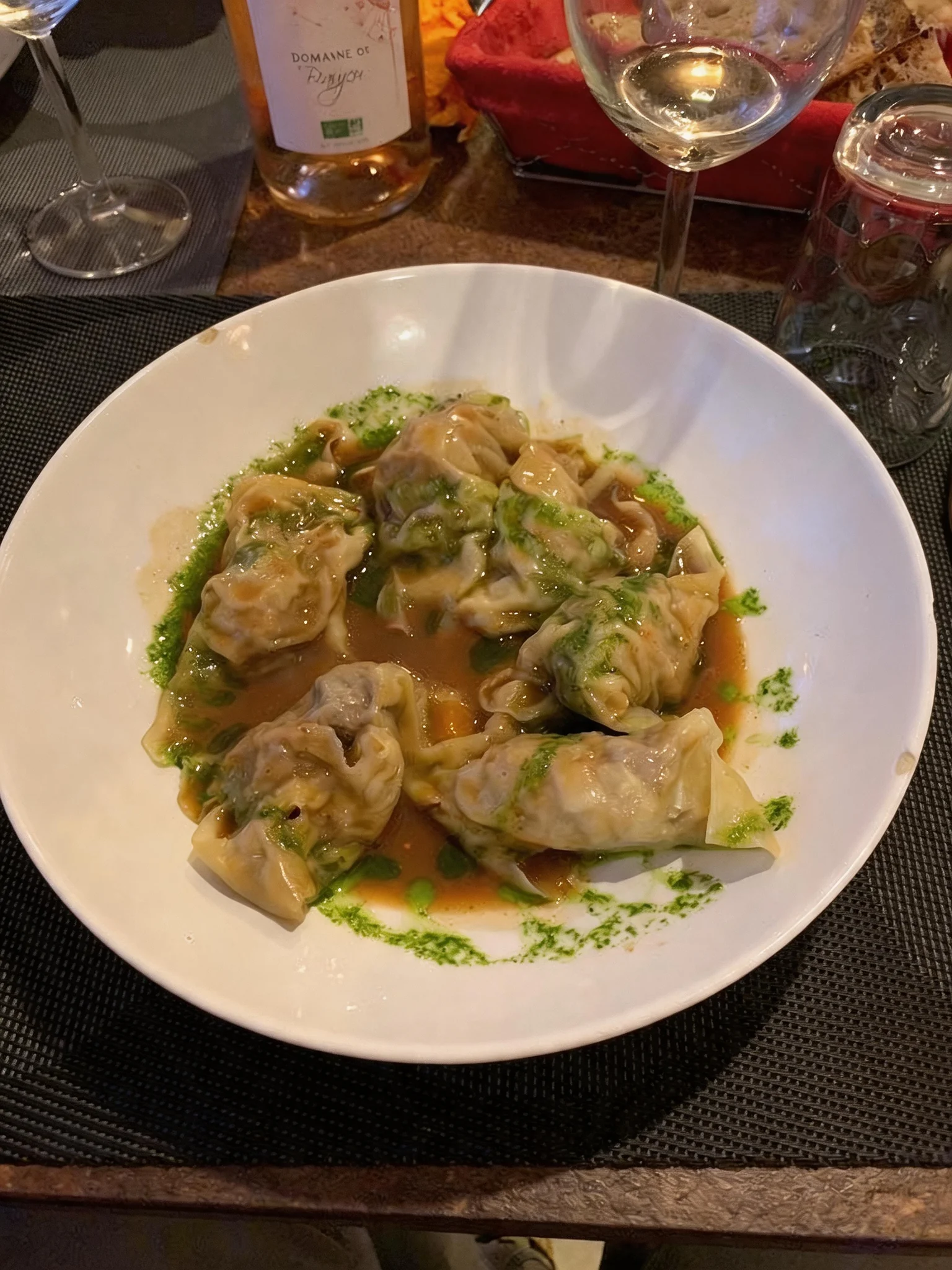 A plate of ravioli in broth, set on a table with a glass of wine.